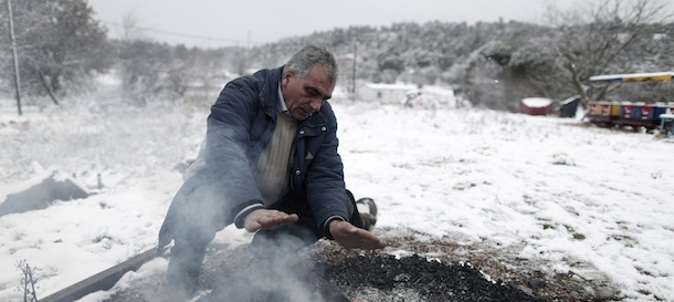 Fairground owner Yannis Kasternopoulos warms himself over an open woodfire as snow blankets his grounds in Stamata, on the northern fringes of Athens, on Tuesday, Jan, 8, 2013. Greece, which is struggling with its worst financial crisis in decades, suffered a sudden cold snap Tuesday, with freezing temperatures in much of the country and snow falling even in central Athens. (AP Photo/Petros Giannakouris)