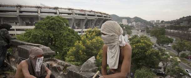 Two masked men keep a lookout on the rooftop an old Indian museum, in Rio de Janeiro, Brazil, Saturday, Jan. 12, 2013. Police in riot gear on Saturday surrounded the site in preparation for the eviction of an indigenous settlement of men and women living on the grounds of the old museum . The settlement is next to the Maracana stadium, pictured left in background, which is being refurbished to host the opening and closing ceremonies of the 2016 Olympics and the final match of the 2014 World Cup. Authorities say the compound must go as the area around the stadium is also being refurbished, expected to be transformed into a shopping and sports entertainment hub. (AP Photo/Felipe Dana)