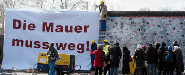 German comedian Tobias Schlegl takes part on an action next to a banner "Die Mauer muss weg" (The Wall must Go) at the East Side Gallery part of the remains of the former Wall in Berlin on March 26, 2013 in Berlin. Some 25 meters of this section of the wall that mostly came down 23 years ago and marked the end of the cold war is to be taken away to make way for a new housing development on river Spree. AFP PHOTO / JOHANNES EISELE (Photo credit should read JOHANNES EISELE/AFP/Getty Images)