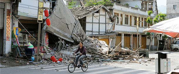 In this photo released by China's Xinhua News Agency, a local resident bicycles in front of collapsed houses after an earthquake struck in Lushan County, Ya'an City, in southwest China's Sichuan Province, Saturday, April 20, 2013. A powerful earthquake struck the steep hills of China's southwestern Sichuan province Saturday morning, leaving at least 160 people dead and more than 6,700 injured. (AP Photo/Xinhua, Jin Xiaoming) NO SALES