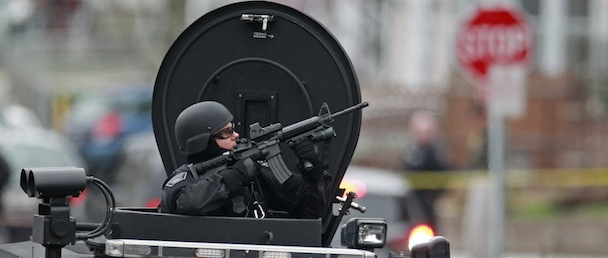 Police in tactical gear arrive on an armored police vehicle as they surround an apartment building while looking for a suspect in the Boston Marathon bombings in Watertown, Mass., Friday, April 19, 2013. The bombs that blew up seconds apart near the finish line of the Boston Marathon left the streets spattered with blood and glass, and gaping questions of who chose to attack and why. (AP Photo/Charles Krupa)