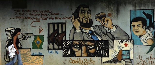 SAO PAULO, BRAZIL: A passer-by walks in front of a grafitti painted on the wall of the former Carandiru prision complex, representing criminal situations with a phrase (L-top) that reads "On the other side of the wall, what the system can cause...on this side what 'it' can not avoid!", the day after the worst wave of violence, in downtown Sao Paulo, Brazil, 17 May 2006. South America's biggest city has been gripped by fear since a powerful gang launched attacks on police stations, banks and buses, and prison uprisings. Authorities have ordered an increased police presence in sensitive areas of the metropolis of 20 million people. The death toll in a criminal gang offensive soared to 133 after a fourth night of attacks and the discovery of bodies at a prison. AFP PHOTO/Mauricio LIMA (Photo credit should read MAURICIO LIMA/AFP/Getty Images)