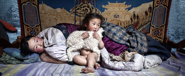 Asia, Mongolia. 19/03/2011. In the photo Erdene Tuya together with her 3 years old son called Tuvchinj (he hugs a young sheep which sleeps with them) just woke up while her husband Batgargal went out to have a look at the herd with the other son called Azjargal, 6 years old. In Mongolia's Arkhangai province, the Tsamba family lives on the edge, struggling through harsh winters alongside their herd of sheep. Severe winter conditions, known as dzud, have been responsible for the deaths of half the family's once 2,000-strong herd over the past three winters. Recently, in search of warmer pastures, the Tsambas moved from Bulgan province in the north to this region near a central Mongolian village called Ulziit. Only in 2010, during one of the harsher Dzuds, more than 8 million sheep, cows, horses and camels died in Mongolia so 39,000 herdsmen had no choice but to migrate towards Ulan Bator.
TEXT:
Mongolia, with its 3.000.000 inhabitants, is an extremely poor country where 20% of the population live on 1,25 dollars a day and 30% suffer from malnutrition. Almost half of the population lives on top of each other in the capital, Ulaan Baator, which hosts over 1.200.000 citizens. Most of them lives in the slum which has developed around the city known as âGher Districtâ. It takes the name from the traditional Mongolian tents the herdsmen abandoning the rural areas bring with them, being the only property they have left.
The climate changes this country is experiencing reinforce an already dramatic social situation and pose a serious challenge for the pride and identity of a nation which finds its roots in the nomadic lifestyle. 
With the Dzud, the hard Mongolian winter, becoming longer and snowier, thousands of nomad herdsmen, who saw their animals die of cold (temperatures reaching -50Â°), were forced to move their Gher to follow the abundance of the pastures or to migrate towards the capital. These people share a common destiny: severe winter conditions undermined the