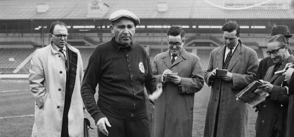 Benfica coach and manager Bela Guttmann (1900 - 1981) with a group of journalists at White City in London, 4th April 1962. He had just accused Tottenham Hotspur of watering the pitch at White Hart Lane, in preparation for their game against Benfica the next day. The match was the second leg semi-final of the European Cup. (Photo by Keystone/Hulton Archive/Getty Images)