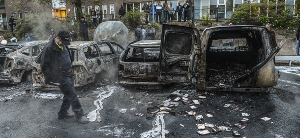 A passerby checks out burn cars in the Stockholm suburb of Rinkeby after youths rioted in several different suburbs around Stockholm for a fourth consecutive night, late May 23, 2013. Youths in immigrant-heavy Stockholm suburbs torched cars and threw rocks at police in riots believed to be linked to a deadly police shooting of a local resident in the suburb of Husby. (AP Photo/Scanpix, Fredrik Sandberg) SWEDEN OUT