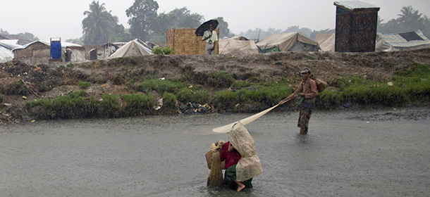 Internally displaced Rohingya man walks across a stream with a child in his back as another catch fish with a net alongside makeshift tents in a camp for Rohingya people in Sittwe, northwestern Rakhine State, Myanmar, ahead of the arrival of Cyclone Mahasen, Tuesday, May 14, 2013. The U.N. said the cyclone, expected later this week, could swamp makeshift housing camps sheltering tens of thousands of Rohingya. Myanmar state television reported Monday that 5,158 people were relocated from low-lying camps in Rakhine state to safer shelters. But far more people are considered vulnerable. (AP Photo/Gemunu Amarasinghe)