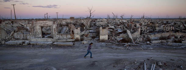 In this May 6, 2013 photo, former resident and tourist guide Norma Berg walks by a street in Epecuen, a village that once was submerged in water in Argentina. People come to see the rusted hulks of automobiles and furniture, crumbled homes and broken appliances. They climb staircases that lead nowhere, and wander through a graveyard where the water toppled headstones and exposed tombs to the elements. (AP Photo/Natacha Pisarenko)
