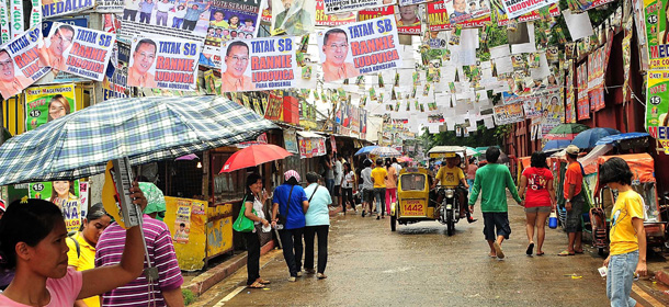 MANILA, PHILIPPINES - MAY 13: Voters walk beneath election posters, suspended over a street in a polling precinct May 13, 2013 in Manila, Philippines. Millions of Filipinos are heading out to cast their votes for the mid-term election today. So far, over 50 people have been killed in the run up to polling day for the elections that have been marred by violence and accusations of corruption and neopotism. (Photo by Veejay Villafranca/Getty Images)