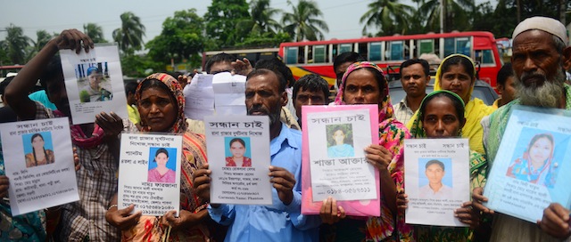 Bangladeshi family members hold up portraits of missing relatives believed to have died at the site of the April 2013 nine-storey building collapse in Savar, on the outskirts of Dhaka on May 24, 2013. Some 290 unidentified bodies were buried after DNA samples were collected to match those of relatives as the Bangladeshi army wrapped up its search May 14, 2013 for bodies at the site of the building collapse. Industrial disasters since November have killed at least 1,250 workers, highlighting the appalling safety problems in the plants where three million workers toil for a basic monthly wages of USD 40, among the world's lowest. AFP PHOTO/ Munir uz ZAMAN (Photo credit should read MUNIR UZ ZAMAN/AFP/Getty Images)