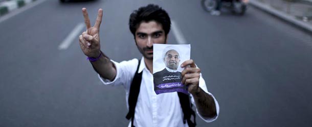 A supporter of the Iranian presidential candidate Hasan Rowhani, a former Iran's top nuclear negotiator, flashes a victory sign, as he holds his poster, in a street campaign, in Tehran, Iran, Tuesday, June 11, 2013. The presidential election will be held on June 14. (AP Photo/Ebrahim Noroozi)
