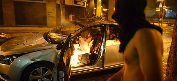 A masked vandal is seen next to a vehicle set on fire during clashes in Rio de Janeiro's downtown, on June 17, 2013. Tens of thousands of people took to the streets of major Brazilian cities protesting the billions of dollars spent on the Confederations Cup --and preparations for the upcoming World Cup-- and against the hike in mass transit fares. AFP PHOTO / CHRISTOPHE SIMON (Photo credit should read CHRISTOPHE SIMON/AFP/Getty Images)