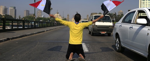 A man waves Egyptian flags as he kneels on a bridge that leads to Tahrir Square in Cairo, Egypt, Friday, July 26, 2013. Political allies of Egypt's military lined up behind its call for huge rallies Friday to show support for the country's top general, pushing toward a collision with Islamist opponents demanding the return of Mohammed Morsi, the nation's ousted president. (AP Photo/Hassan Ammar)
