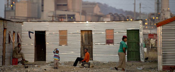 People sit outside their shacks on July 9, 2013 in the Nkaneng shantytown next to the platinum mine, run by British company Lonmin, in Marikana. On August 16, 2012, police at the Marikana mine open fire on striking workers, killing 34 and injuring 78, during a strike was for better wages and living conditions. Miners still live in dire conditions despite a small wage increase. AFP PHOTO / ODD ANDERSEN (Photo credit should read ODD ANDERSEN/AFP/Getty Images)