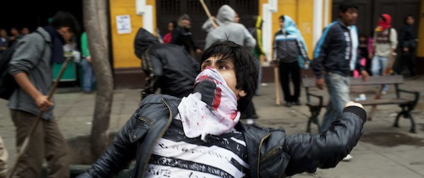 A man throws a stone towards riot policemen during a protest against the new civil service law that will require government employees to undergo work evaluations, in Lima, Peru, Thursday, July 4, 2013. After hours of debates and months of modifications, Peru's Congress approved the new civil service law with 59 votes in favor, 45 against and 3 abstentions. (AP Photo/Rodrigo Abd)