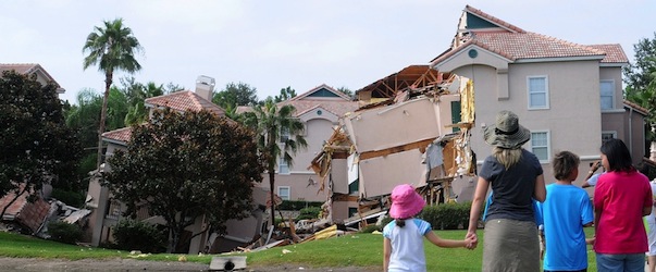 CLERMONT, FL - AUGUST 12: People look at a partially collapsed building over a sinkhole at Summer Bay Resort near Disney World on August 12, 2013 in Clermont, Florida. The 40 to 60 foot sinkhole opened up under the resort building reportedly begining late August 11 into early August 12. There were no injuries or deaths reported. (Photo by Gerardo Mora/Getty Images)