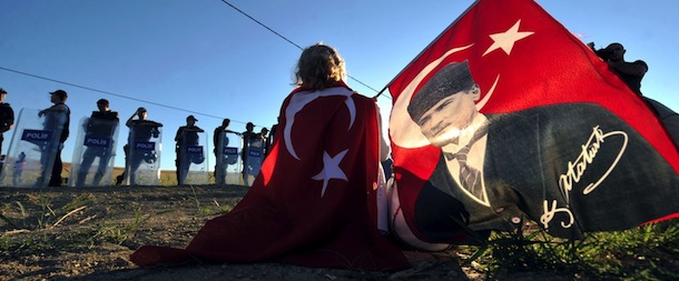 Wrapped in a Turkish flag and holding another one with a portrait of Mustafa Kemal Ataturk, a protestor sits in front of police forces blocking the access to a courthouse in Silivri, near Istanbul, on August 5, 2013, where clashes erupted after a court decision to sentence a former army chief and other top brass to life in prison in a high-profile trial of 275 people accused of plotting to overthrow the Islamic-rooted government. Ex-military chief Ilker Basbug, along with several other army officers, were sentenced to life in prison, while 21 people were acquitted, according to the verdicts issued so far. The trial has been seen as as a key test in Prime Minister Recep Tayyip Erdogan's showdown with secularist and military opponents during his decade-long rule. AFP PHOTO / OZAN KOSE (Photo credit should read OZAN KOSE/AFP/Getty Images)