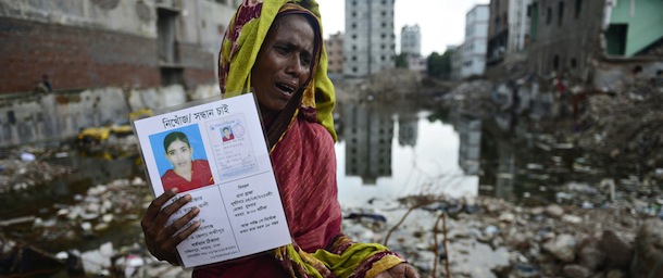 A mourner holds up a portrait of her missing relative (L), presumed dead following the April 24 Rana Plaza garment building collapse, and a bone fragment (R) believed to be from one of the many unidentified remains of killed garment workers, at the scene on the one hundredth-day anniversary of the disaster in Savar, on the outskirts of Dhaka, on August 2, 2013. Hundreds of garment workers staged demonstrations at the site of Bangladesh's worst industrial disaster, demanding compensation for the survivors and a full account of the missing labourers of the April 24, 2013 factory building collapse that killed 1,129 people. AFP PHOTO/ Munir uz ZAMAN (Photo credit should read MUNIR UZ ZAMAN/AFP/Getty Images)
