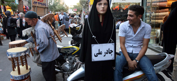 An Iranian boy wears western style clothes as he sits next to a mannequin with a sign that reads "national chador" (veil) in an open market in south Tehran, Iran on Sept. 16, 2007. The shops in north Tehran are full of Western pop music and movies _ the latest Harry Potter film, even 'The Simpsons'. Young women stroll the streets in skinny jeans and short coats, their heads barely covered, arm-in-arm with boys in muscle shirts and spiky hair. It is the paradox of Tehran today _ a city and people surprisingly cosmopolitan and far different from Western stereotypes, paired with an ultraconservative government working to consolidate its power and at sharp odds with the West. (AP Photo/Hasan Sarbakhshian)