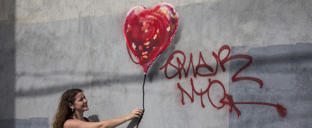 NEW YORK, NY - OCTOBER 07: A woman poses with a piece of street art, which depicts a heart-shaped balloon covered in bandages and was allegedly done by the street artist Banksy, on October 7, 2013 in the Red Hook neighborhood of the Brooklyn borough of New York City. The piece was defaced with red spray paint shortly after being completed. (Photo by Andrew Burton/Getty Images)