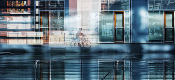 A person rides with a bicycle alongside the river Spree as it is photographed trough multiple reflections of windows at a courtyard of a parliament office building in Berlin Monday, Oct. 14, 2013. AP Photo/Markus Schreiber)