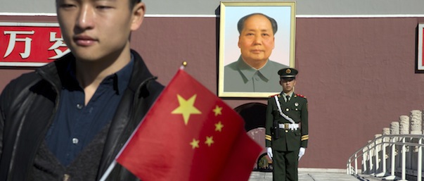 A tourist holds up a Chinese flag as he poses for photos near a Chinese paramilitary policeman on duty in front of former Chinese leader Mao Zedong&#8217;s portrait on Tiananmen Gate, close to the site of an incident Monday where a car plowed through a crowd before it crashed and burned in Beijing, China, Tuesday, Oct. 29, 2013. Police investigating the apparent car attack at Beijing&#8217;s Forbidden City searched Tuesday for information on two ethnic Uighur minority suspects, a hotel employee said, a day after the incident which killed five people and injured 38.(AP Photo/Ng Han Guan)
