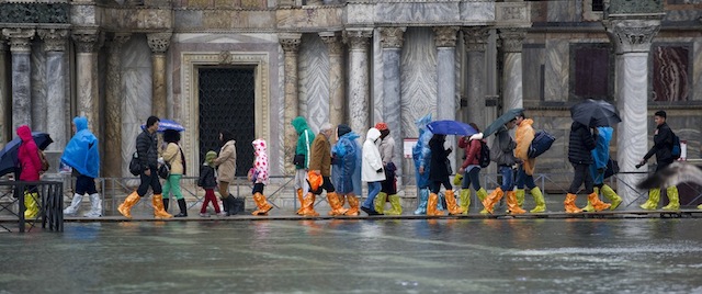 VENICE, ITALY - NOVEMBER 19: Tourists wearing coloured boots walk under heavy rain and wind in a flooded Saint Mark's Square during high waters on November 19, 2013 in Venice, Italy. Venice will be affected by the high water for the next few days due to the passage of Cyclone Cleopatra that hit the Italian island of Sardinia causing devastating flooding, which has left at least 17 dead. (Photo by Marco Secchi/Getty Images)