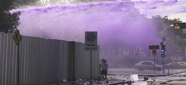 A man shield himself as riot police shoots water cannon at anti-government protesters at a gymnasium in Bangkok, Thursday, Dec. 26, 2013. Protesters trying to halt preparations for elections fought running battles with police in the Thai capital on Thursday, escalating their campaign to topple the country's beleaguered government. (AP Photo/Sakchai Lalit)