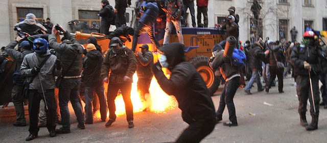 A stun grenade explodes between protesters as they clash with police during the storming of the Viktor Yanukovych Presidential office in Kiev during a mass rally of the opposition in Kiev on December 1, 2013. The crowd chanted "Revolution!" and "Down with the Gang" as it took control of Kiev's iconic Independence Square and steered a bulldozer within striking distance of police barricades protecting the nearby presidential adminstration office. AFP reporters saw security forces outside the presidential building fire stun grenades and smoke bombs at a few dozen masked demonstrators who were pelting police with huge stones and what Ukrainian media said were molotov cocktails. AFP PHOTO/GENYA SAVILOV (Photo credit should read GENYA SAVILOV/AFP/Getty Images)