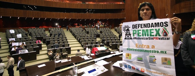 An opposition lawmaker holds a sign that reads in Spanish: "we defend Pemex" as he occupies the podium at the National Congress in protest against the newly approved energy reform bill in Mexico City, Wednesday, Dec. 11, 2013. Mexico's Senate, the early hours of Wednesday approved the most dramatic oil reform in decades, moving the country closer to opening its state-run sector to private companies and investment. (AP Photo/Marco Ugarte)