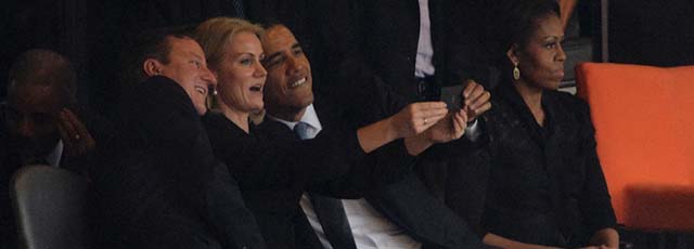 US President Barack Obama (R) and British Prime Minister David Cameron pose for a picture with an unidentified official next to US First Lady Michelle Obama (R) during the memorial service of South African former president Nelson Mandela at the FNB Stadium (Soccer City) in Johannesburg on December 10, 2013. Mandela, the revered icon of the anti-apartheid struggle in South Africa and one of the towering political figures of the 20th century, died in Johannesburg on December 5 at age 95. AFP PHOTO / ROBERTO SCHMIDT (Photo credit should read ROBERTO SCHMIDT/AFP/Getty Images)