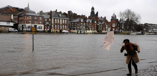 A woman struggles with her umbrella as rising water levels from the River Ouse bring floodwater into riverside roads in York, England, as heavy rain and strong winds sweep across many parts of Britain, Monday Dec. 23, 2013. (AP Photo/PA, John Giles) UNITED KINGDOM OUT NO SALES NO ARCHIVE