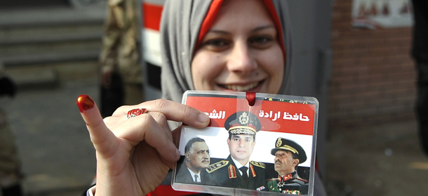 An Egyptian woman shows her ink-stained finger as she holds a card bearing portraits of late Egyptian presidents Gamal Abdel Nasser (L) and Anwar Sadat (R) alongside Egypt's Defence Minister army chief Abdel Fattah al-Sisi (C), with text reading in Arabic: "Protector of the people's will", after casting her ballot at a polling station during the second day of voting on a new constitution on January 15, 2014 in the northern port city of Alexandria. Egyptians resumed voting in the constitutional referendum, with turnout expected to hold the key to a likely presidential bid by army chief Abdel Fattah al-Sisi after clashes killed nine the previous day. AFP PHOTO / STR (Photo credit should read STR/AFP/Getty Images)