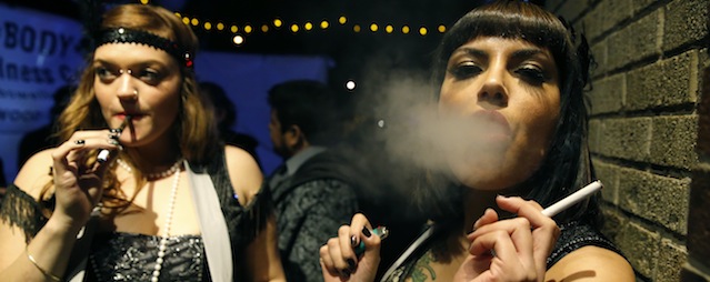 Partygoers smoke marijuana, left, and cigarettes during a Prohibition-era themed New Year's Eve party celebrating the start of retail pot sales, at a bar in Denver, late Tuesday Dec. 31, 2013. Colorado is to begin marijuana retail sales on Jan. 1, a day some are calling ‘Green Wednesday.' (AP Photo/Brennan Linsley)