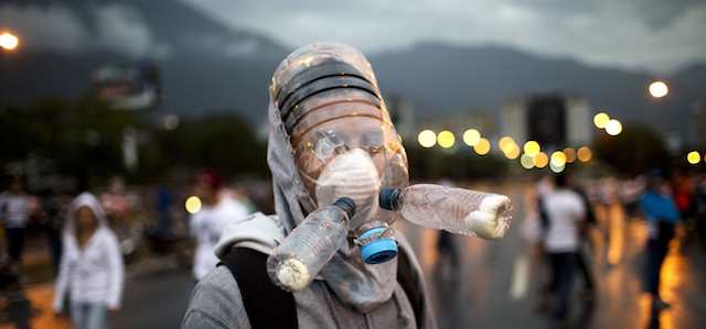 A protester wearing a gas mask made from plastic water bottles poses for a picture during an opposition protest blocking a highway outside La Carlota airport in Caracas, Venezuela, Tuesday, Feb. 18, 2014. Members of the opposition are protesting after their leader Leopoldo Lopez surrendered to authorities Tuesday. Lopez was being sought by authorities for allegedly inciting violence during protests last week in which three people were killed as government forces clashed with protesters. (AP Photo/Rodrigo Abd)