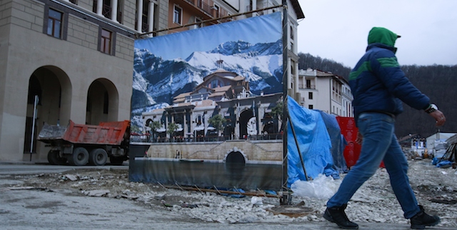 A worker enters a construction site behind a decorate fence next to accommodation for the Sochi 2014 Winter Olympics, Saturday, Feb. 1, 2014, in Krasnaya Polyana, Russia. According to the Sochi Olympic organizing committee, only six of the nine media hotels in the mountain area are fully operational. The accommodation for athletes, however, has not been affected by the problems. (AP Photo/Gero Breloer)