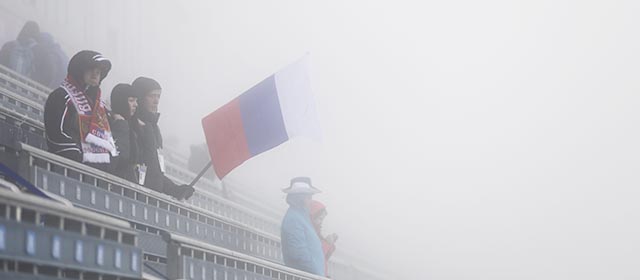 Spectators with a Russian flag stand in thick fog on the stands prior to the men's biathlon 15k mass start, at the 2014 Winter Olympics, Monday, Feb. 17, 2014, in Krasnaya Polyana, Russia. The men’s 15-kilometer mass-start biathlon race at the Sochi Olympics has been delayed due to fog, one day after the event had been called off for the same reason. (AP Photo/Gero Breloer)