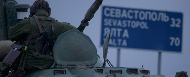 A soldier rests atop a Russian armored personnel carriers with a road sign reading "Sevastopol - 32 kilometers, Yalta - 70 kilometers", near the town of Bakhchisarai, Ukraine, Friday, Feb. 28, 2014. The vehicles were parked on the side of the road near the town of Bakhchisarai, apparently because one of them had mechanical problems. (AP Photo/Ivan Sekretarev)