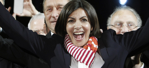French Socialist Party deputy mayor of Paris, Anne Hidalgo, center, smiles, as outgoing mayor Bertrand Delanoe, stands behind her, during a speech after results were announced in the second round of the French municipal elections, in Paris, Sunday, March 30, 2014. Hidalgo saved Paris for the flagging Socialist Party in Sunday's municipal elections, becoming the French capital's first female mayor. (AP Photo/Thibault Camus)