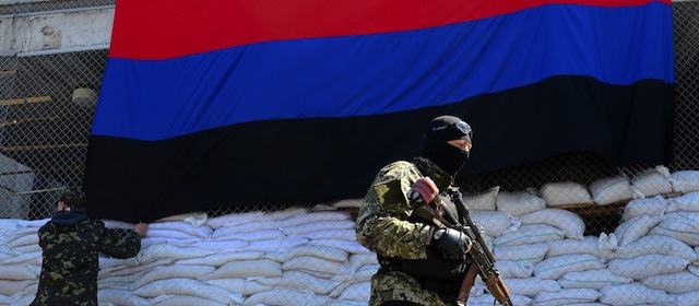 An armed man in military fatigues stands guard as two men hang the flag of the so-called "People's Republic of Donetsk" outside the regional administration building in the eastern Ukrainian city of Slavyansk on April 21, 2014. US Vice President Joe Biden was to begin a two-day visit to Ukraine amid Russian "outrage" over a deadly weekend shootout in the rebel east that shattered a fragile Easter truce. Washington has warned Moscow that time is running out for the implementation of an accord signed along with Ukraine and the European Union in Geneva that was meant to ease tensions in the crisis-hit country. AFP PHOTO/KIRILL KUDRYAVTSEV (Photo credit should read KIRILL KUDRYAVTSEV/AFP/Getty Images)