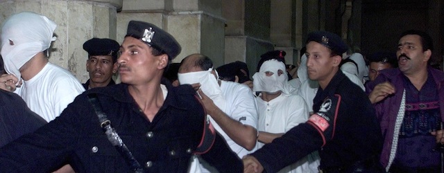 CAIRO, EGYPT: Egyptians dressed in white with their faces covered, charged with engaging in homosexual activities and scorning Islam, enter a Cairo court under the protection of security men 14 November 2001. One of the 52 men was sentenced to five years in prison and several to three years at the end of their trial. The men were arrested in May following a party on a Nile riverboat. AFP PHOTO/Marwan NAAMANI (Photo credit should read MARWAN NAAMANI/AFP/Getty Images)