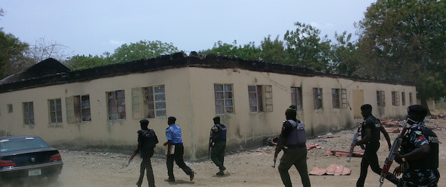 In this photo taken Monday, April, 21. 2014. Security walk past burned government secondary school Chibok, were gunmen abducted more than 200 students in Chibok, Nigeria. Nigerian parents say more than 200 girls and young women abducted from the Chibok school by Islamic militants remain missing one week later, despite a "hot pursuit" by security forces and an independent search by desperate parents who went into a dangerous forest. Dozens of the kidnapped girls managed to escape by jumping from the back of an open truck or hiding in dense forest. (AP Photo/ Haruna Umar)
