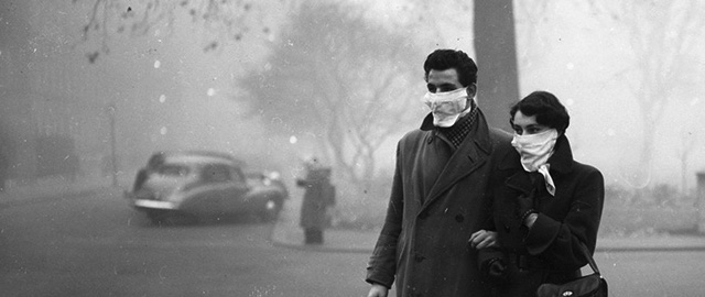 November 1953: A couple walking in London wearing smog masks on a foggy day. (Photo by Monty Fresco/Topical Press Agency/Getty Images)