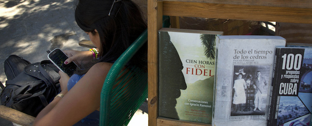 A book street vendor passes the time on her smart phone as she waits for customers in Havana, Cuba, Tuesday, April 1, 2014. The Obama administration secretly financed a social network in Cuba to stir political unrest and undermine the country’s communist government according to an Associated Press investigation. The project, dubbed "ZunZuneo," slang for a Cuban hummingbird’s tweet, lasted more than two years and drew tens of thousands of subscribers and sought to evade Cuba’s stranglehold on the Internet with a primitive social media platform. First, the network would build a Cuban audience, mostly young people; then, the plan was to push them toward dissent. (AP Photo/Ramon Espinosa)