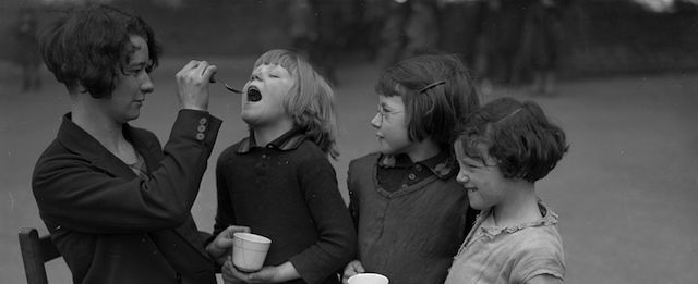 22nd February 1931: A teacher at Sneed Road school gives children a spoonful of medicine to gargle with as a defence against influenza. (Photo by Fox Photos/Getty Images)