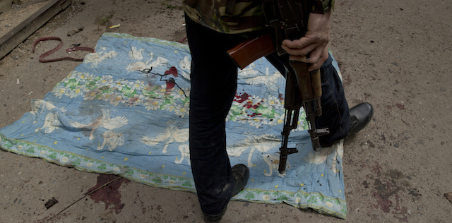 A pro-Russian gunman walks on a sheet stained with the blood of those killed in clashes with Ukrainian government forces around the airport outside a city morgue in Donetsk, Ukraine, Tuesday, May 27, 2014. The eastern city of Donetsk was in turmoil Tuesday a day after government forces used fighter jets to stop pro-Russia separatists from taking over the airport. Dozens were reported killed and the mayor went on television to urge residents to stay indoors. (AP Photo/Vadim Ghirda)
