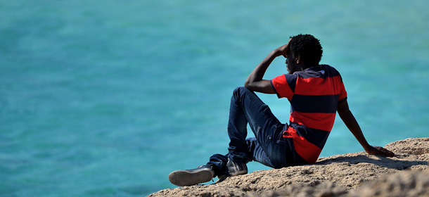 A migrant sits on rocks and stares at the sea in Lampedusa island on October 26, 2013. There are currently three navy vessels on patrol, along with six coast guard patrol boats and six border guard patrol boats, as well as helicopters and planes from each of the three agencies patrolling the area as part of the new 'Mare Nostrum' surveillance and rescue operation, launched after more than 400 migrants drowned in two disasters earlier this month. Nearly 800 refugees were rescued off Sicily in several operations as European leaders grapple with the issue of illegal immigration at a European Union summit. AFP PHOTO /Filippo MONTEFORTE (Photo credit should read FILIPPO MONTEFORTE/AFP/Getty Images)