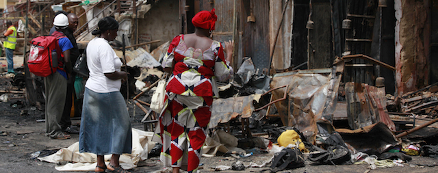 People gather at the site of Tuesday's car bombs in Jos, Nigeria, Wednesday, May 21, 2014. Two car bombs exploded at a bustling bus terminal and market in Nigeria's central city of Jos on Tuesday, killing over 100 people, wounding dozens and leaving bloodied bodies amid the flaming debris. There was no immediate claim of responsibility for the twin car bombs. (AP Photo/Sunday Alamba)