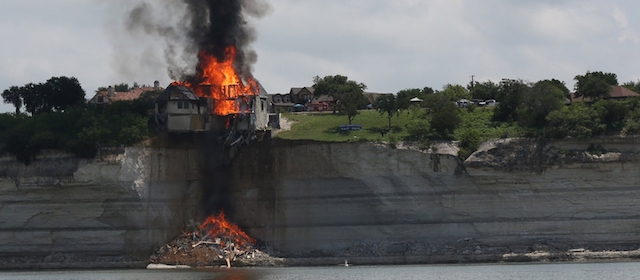 A $700,000 vacation home perched on a crumbling cliff overlooking Lake Whitney is engulfed by fire as demolition crews wait for the structure to burned to the ground deliberately Friday, June 13, 2014, near Whitney, Tx. The house was condemned earlier after a fracture appeared in the bluff on which it was built. (AP Photo/Waco Tribune Herald, Rod Aydelotte)
