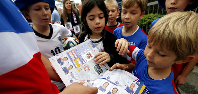 Flavio Aquino, of San Diego, holds up a sticker book with portraits of the United States men's soccer team players as children gather around outside of the Sao Paulo FC training center where the U.S. is holding its training in Sao Paulo, Brazil, Wednesday, June 11, 2014. The U.S. will play in group G of the 2014 soccer World Cup. (AP Photo/Julio Cortez)