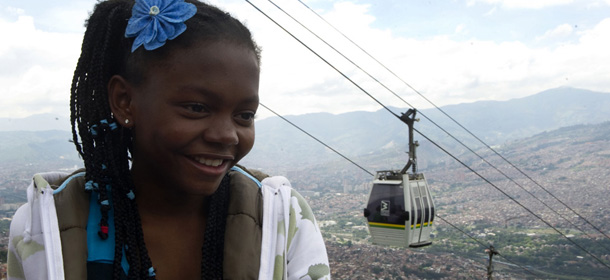 A girl smiles with the Metrocable behind her, in Santo Domingo Savio neighbourhood in Medellin, Antioquia department, Colombia on March 1, 2013. Medellin, which competed with New York and Tel Aviv, was chosen by popular vote through the internet, as the ?Innovative City of the Year? during the City of the Year contest, organized by The Wall Street Journal and Citigroup. The distinction was basically made for its modern transportation system, its public library, escalators built in a shantytown and schools that have allowed the integration of society. AFP PHOTO/Raul ARBOLEDA (Photo credit should read RAUL ARBOLEDA/AFP/Getty Images)